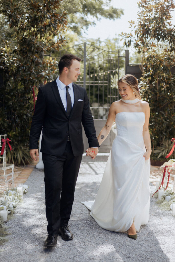A bride and groom waling in the courtyard at the Supposey Warehouse & Gardens wedding venue, holding hands.
