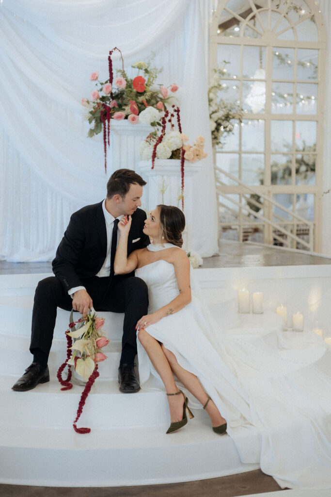 A bride and groom sitting on the steps in the warehouse of the Supposey Warehouse & Gardens wedding venue. 