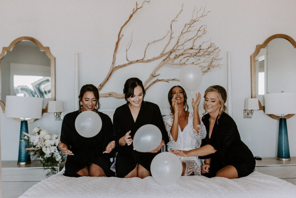 bride and bridesmaids playing with balloons on a bed