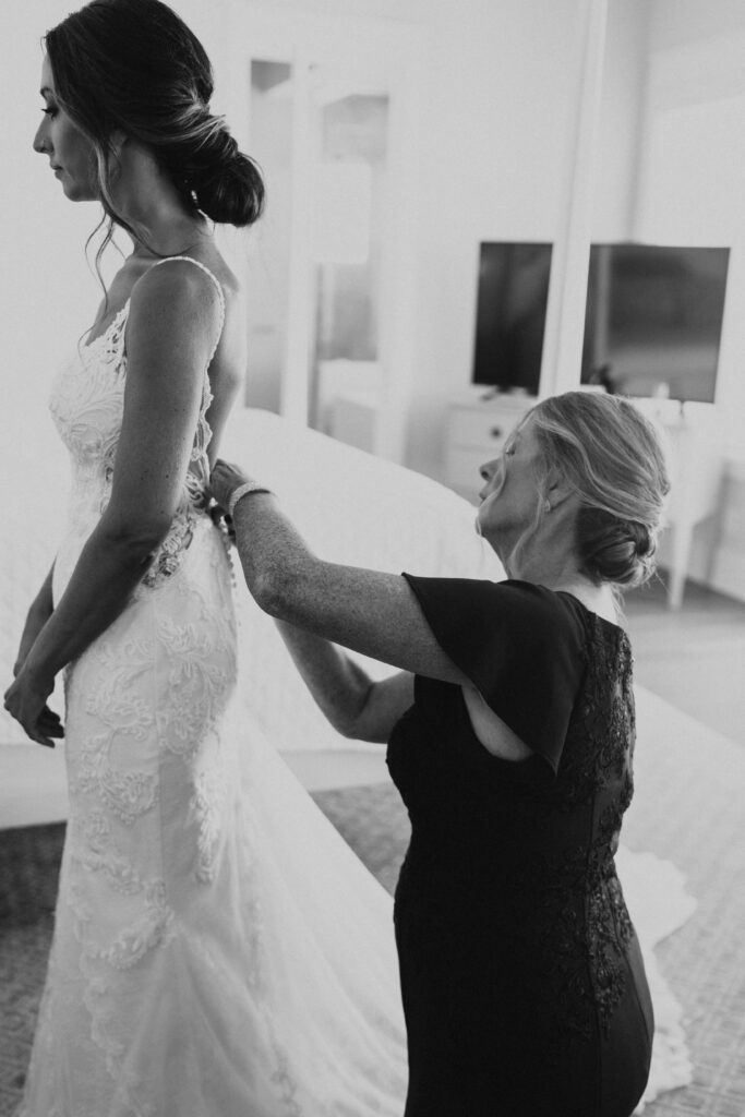 black and white photo of mom zipping up bride's dress