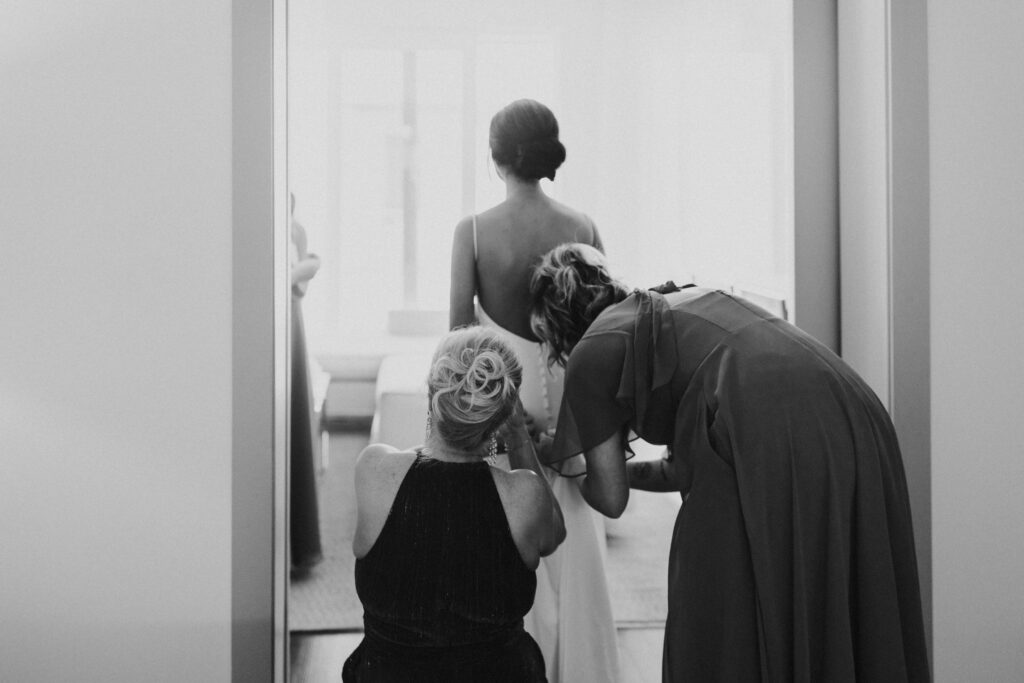 Bridesmaid and mom adjusting brides dress