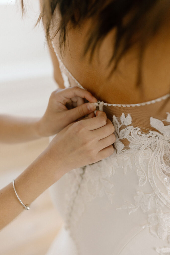 Daughter buttoning bride's wedding gown