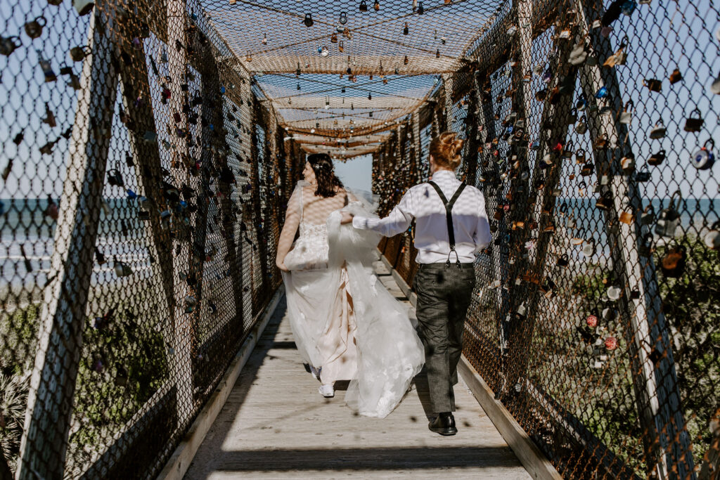 Bride and groom walking down a lovelock bridge to the beach