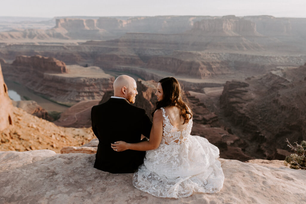 a couple sitting on the edge of a cliff at dead horse point state park